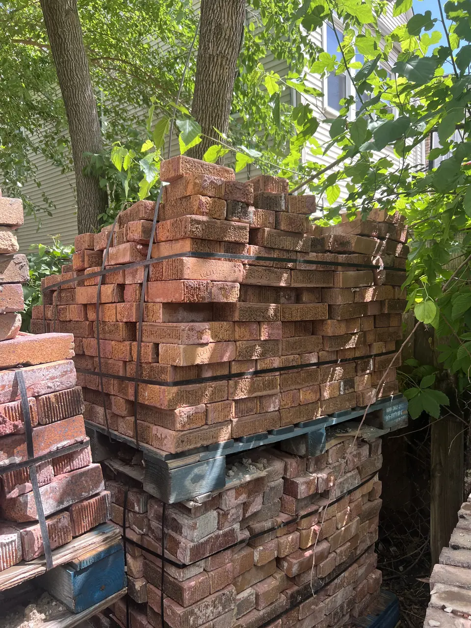 Tall stack of reddish reclaimed brick on a pallet outdoors